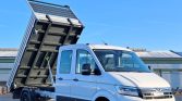 White cab-forward truck with its dump bed raised, ready to unload under a clear blue sky.