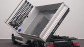 White truck with a metal tipping dump bed raised for unloading in a studio setting