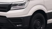Close-up of a white van's front left corner showing the headlight, bumper, and front wheel with a black steel rim.