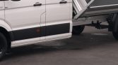 White cargo truck with a raised metal dump bed on the right, black lower body panel, and orange side marker.