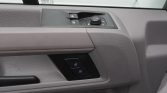 Close-up of a gray car door interior with window/lock controls and a round mirror-adjustment dial on the armrest panel.