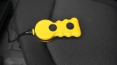 Yellow plastic handheld device with two black circular buttons on a car seat, connected by a short cord.