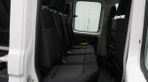 Interior of a white van showing a row of black fabric seats with headrests, seen from the open side door.
