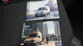 Two MAN van brochures on a car seat—one shows a silver van and 'WARTUNGSNACHWEIS'; the other, a tan van in a city setting labeled 'readme'.