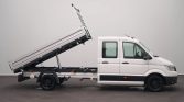 White dual-cab pickup with a raised tilting cargo bed for dumping load-ed, viewed from the side.