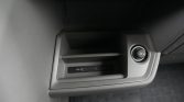 Car interior: center console with a 12V power outlet and USB ports panel beside a small shelf area.