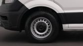 Front wheel of a white van, showing a silver steel rim and black tire with part of the bumper nearby.