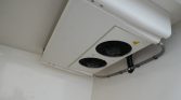 White outdoor HVAC unit with two circular fan grills mounted on a wall/ceiling, with conduit running along the pipe toward the right.