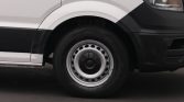 Front left wheel and tire of a white van, showing a steel wheel and black wheel arch trim, visible on pavement.