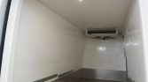 Empty white refrigerated trailer interior with diamond-plate metal trim along lower walls and a ceiling-mounted cooling unit