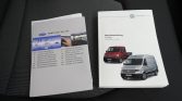 Two VW vehicle manuals on a car seat: a gray Vento manual and a white Crafter manual with red and silver vans.