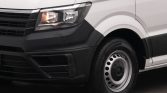 Close-up of a white van's front left corner, displaying the headlight, black bumper, and steel wheel with hubcap