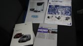Sheet of vehicle manuals laid on a car seat: Carrier ‘Cool by Carrier’ product sheet and an ‘Original’ mounting kit booklet, plus two VW/Kasten van manuals and a multilingual operator manual in gray cover.