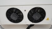 Two large circular cooling fans on an outdoor HVAC condenser unit, with wiring and a yellow warning label nearby.