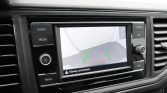 In-car infotainment screen showing a rearview camera view with green guiding lines and a red safety line, dashboard controls around it, warning text in Dutch at the bottom saying 'Rijweg controleren!'