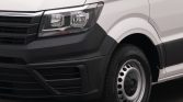 Front left section of a white cargo van showing the headlight, black bumper, and wheel with a steel rim distance.