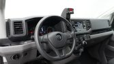 Interior view of a VW van cockpit: steering wheel, instrument cluster, center touchscreen, and manual gear lever from the driver's seat.