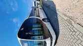 White city bus parked on a cobblestone road under a bright blue sky.