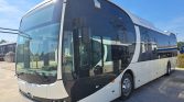 White and black long passenger coach bus parked on a paved lot, front view with large curved windshield and chrome hubcap wheels
