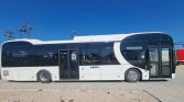 Side view of a modern white bus with large tinted windows parked on a paved area under a clear blue sky.