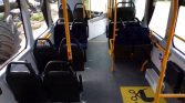 Interior of a public bus with dark blue seats, yellow handrails, and a wheelchair-priority floor marking near the front.