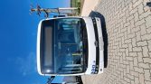 Front view of a white city bus parked on a brick-paved surface under a clear blue sky.