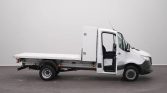 White flatbed tow truck seen from the side with its cab door open, parked indoors.