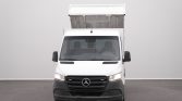 Front view of a white cargo van with a raised dump bed, parked indoors against a gray wall.
