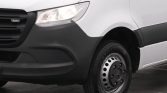 Front-left view of a white cargo van showing the headlight, gray bumper, and wheel with a steel hubcap.