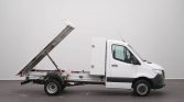 White utility truck with a raised dump bed supported by a hydraulic strut, shown in a studio setting.