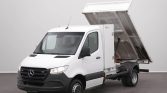 White Mercedes-Benz dump truck with its hydraulic bed raised, ready to unload debris in a facility setting.