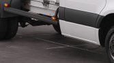 Close-up of a white cargo van showing a black side step extended under the door and orange marker light.