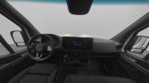 Front interior of a Mercedes van: steering wheel, dashboard with gauges, center touchscreen, gear shift, and front seats viewed from the passenger area.