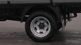 Rear wheel of a truck with a silver steel rim and black tire, on a paved surface nearby the chassis and mudguard edges.