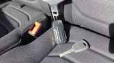Car keys resting on a dark textured car seat with a red seat belt buckle nearby