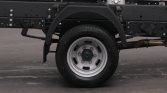 Close-up of a truck wheel and undercarriage, showing the black chassis, tire, and exposed exhaust pipe.