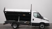White dump truck with its cargo bed raised, shown from the side in a neutral indoor setting.