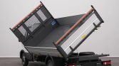 Dump truck with its metal cargo bed raised for unloading in an indoor setting (tilting dump bed)