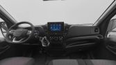 Interior of a modern van dashboard: left-side steering wheel, central touchscreen display, climate controls, and front seats seen from the passenger area.