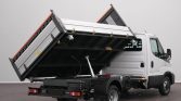 White cab truck with a raised black steel dump bed supported by a hydraulic cylinder, ready to unload on a plain indoor backdrop.