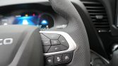Close-up of a car steering wheel showing the right-side cruise control buttons and perforated leather surface