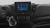 Center-dashboard view of a car with a large touchscreen displaying app icons, climate dials below, and a gear shifter to the left.