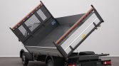 Dump truck with its metal cargo bed raised in a tilted unloading position and open rear gate