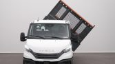 White Iveco truck with a large black tipped cargo bed raised diagonally behind the cab in a neutral showroom setting, orange accents on the bed edge out of view behind the roof.