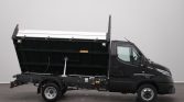 Black cab-forward dump truck with its cargo bed raised in a side profile view, showcasing the hydraulic lifting mechanism and chassis details.