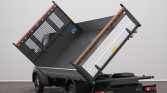 Small utility truck with its metal dump bed raised for unloading, showing taillights and rear branding