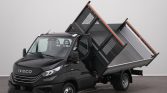 Black Iveco dump truck with raised tipping bed, showing cargo bed tilted upward for unloading in a neutral studio setting.