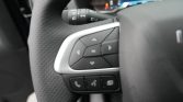 Close-up of a car steering wheel left spoke showing the multi-function control cluster with directional pad, OK button, and a row of phone/menu buttons below.