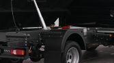 Rear section of a heavy truck trailer showing a vertical hydraulic lift strut, mudguard, wheel, and taillight tail light