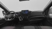 Front interior of a modern van: steering wheel, center touchscreen, climate controls, and gray fabric seats seen from the back seat perspective.
